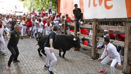 Dos corredores tiran de un Cebada Gago en un encierro del año pasado, con el camión de RTVE para la retransmisión tras el vallado