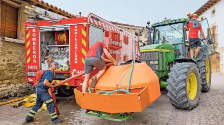 Un bombero ayuda a llenar de agua el depósito del tractor a dos vecinos en Orrio