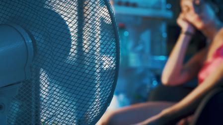 Una mujer intenta refrescarse con un ventilador en una noche tropical durante una ola de calor