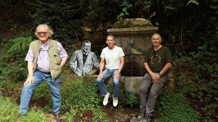 Desde la izquierda, Gerry Dawes, Tim Pinks y Miguel Izu, junto a la fotografía en cartón de Hemingway, colocada en la fuente donde el escritor dejaba a enfriar las botellas de vino, en la Fábrica de armas de Orbaizeta