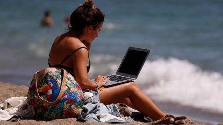 Una mujer consulta su portátil en la playa