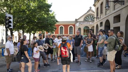 Un gran grupo de turistas, en el que se encuentran María Duran y Marc Paulet, atienden a la explicación de Laura Alonso, su guía, sobre la historia de la ciudad.
