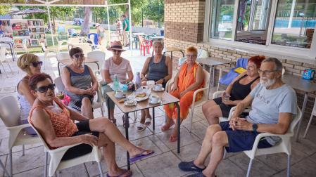De izq. a dcha.: María Antonia Alfaro, Montse Boteargues, María Jesús Ábrego, Inma Bueno, Rufo Ayerbe, Mari Carmen del Río, María José González y Natxo Salinas desayunan en la piscina municipal de Miranda de Arga, con la biblioteca móvil al fondo.