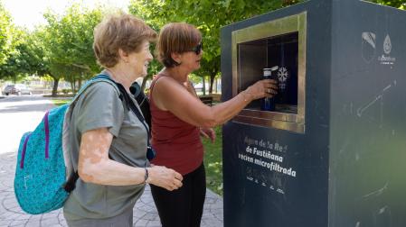 Dos mujeres rellenan una botella de agua en una de las fuentes instaladas en Fustiñana