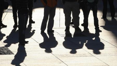 Un grupo de jóvenes reunidos en la calle, cuyas sombras se proyectan en el suelo