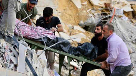 Varias personas transportan un cuerpo entre los escombros causados por un ataque aéreo israelí en Arab Salim