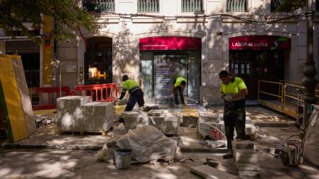 Tres operarios colocan las planchas de hormigón en la acera norte del paseo, junto a una sucursal bancaria y a un bar restaurante