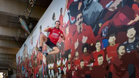 Mikel Recalde recrea el característico salto con el que cierra  sus vídeos frente al mural de Osasuna ubicado en el interior de El Sadar.