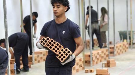 Un alumno traslada unos ladrillos en la escuela taller de albañilería.