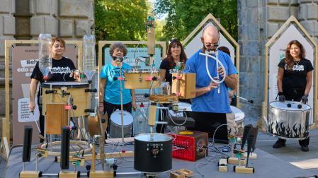 En primer plano, el lutier Jonathan García y su autómata musical elaborado con restos deresiduos de aparatos eléctricos y electrónicos. Detrás, componentes de la batucada BaraBatu.