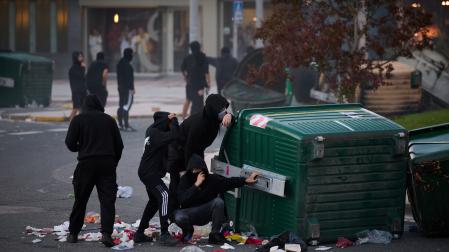 Cuatro manifestantes se protegen detrás de un contenedor volcado junto a la rotonda de la avenida Barañáin con calle Ermitagaña