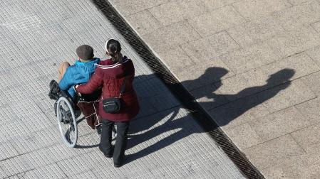Una mujer pasea a una persona en silla de ruedas.