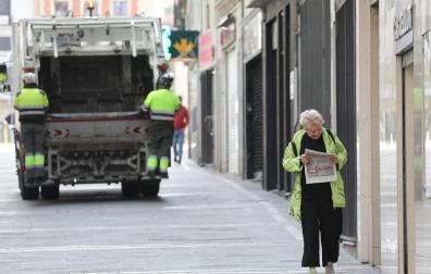 Una mujer regresa de comprar el pan y la prensa en Pamplona. Al fondo, el servicio de recogida de basuras, que sigue funcionando.