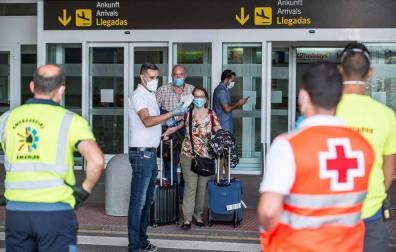 Dos viajeros reciben las indicaciones de los servicios de emergencias tras desembarcar en Lanzarote de un vuelo procedente de Madrid en el que parte del pasaje ha sido sometido a aislamiento después de que uno de los ocupantes del avión diera positivo en covid-19 en unas pruebas cuyos resultados tenía pendiente.