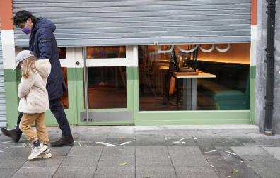 Un hombre y una niña pasan por delante de un establecimiento cerrado en Bilbao.