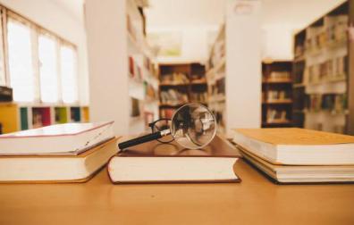 Imagen de una lupa y unas gafas sobre unos libros en la biblioteca