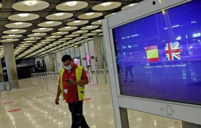 Un operario de Iberia pasa al lado de un monitor con las banderas de España y Reino Unido en la T1 del Aeropuerto de Madrid-Barajas.