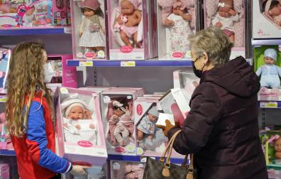 Una dependienta ayuda a una señora ante las estanterías de muñecas