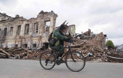 Un ucraniano monta en bicicleta frente a un edificio destruido en Kharkiv, Ucrania