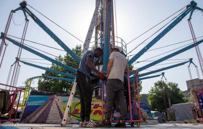 Dos trabajadores desmontan ayer en las barracas la atracción ‘The Limit’ que consiste en sillas voladoras que dan vueltas, suben y bajan