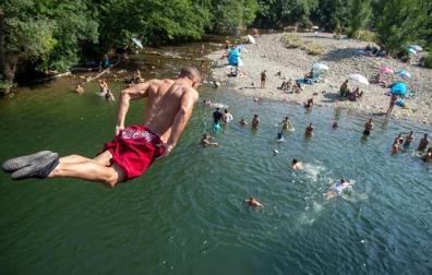 Un joven se lanza al río Arga desde el puente de Irotz, lugar de refresco para muchas personas en esta ola de calor