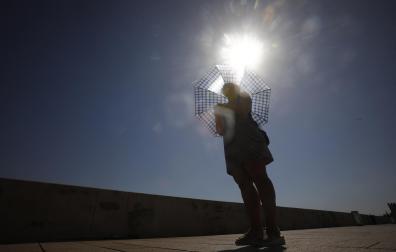 Una mujer se protege del sol con un paraguas mientras pasea por el puente romano de Córdoba
