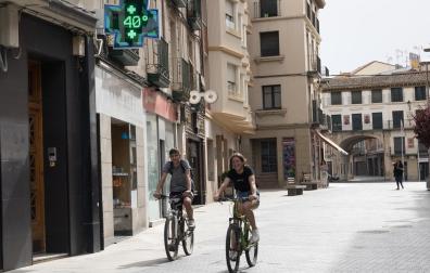 Dos personas pasan con la bici por debajo de un termómetro que marca 40 º en Tudela