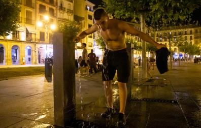 Un joven aprovecha el agua de una de las fuentes de la Plaza del Castillo para refrescarse
