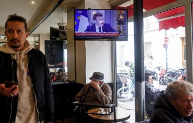 Una televisión en un bar de París muestra la entrevista al presidente francés Emmanuel Macron en la que ha defendido la reforma de las pensiones que aumenta la edad de jubilación de 62 a 64 años
