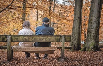 Dos personas mayores descansan en un banco en un paisaje otoñal