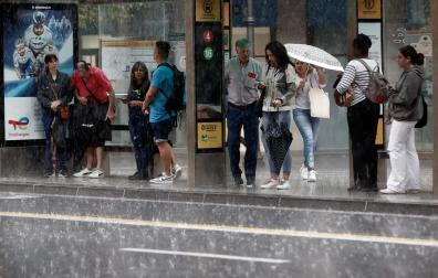 Varias personas se resguardan de la lluvia en una marquesina en Pamplona