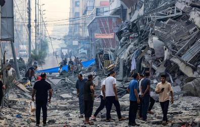 Varias personas hablan junto a los escombros de un edificio derruido por misiles israelíes en Gaza