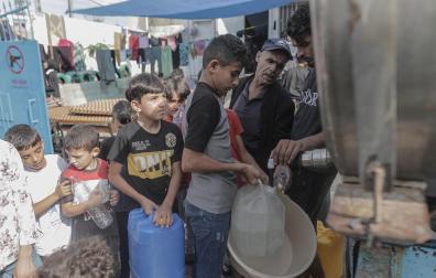 Varios niños palestinos del campamento de Khan Yunis hacen cola para llenar recipientes con agua de un camión cisterna en el sur de la ciudad de Gaza
