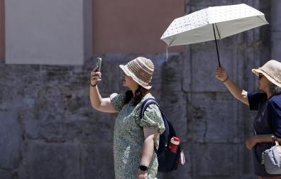 Dos turistas se protegen del sol en Valencia con parasoles y gorros