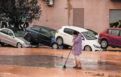 Una mujer limpia junto a coches destrozados en La Torre (Valencia)