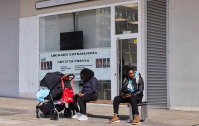Dos personas consultan su móvil en las inmediaciones de la oficina de Extranjería, en el barrio de Buztintxuri. De fondo, un cartel publicita los servicios de un abogado.