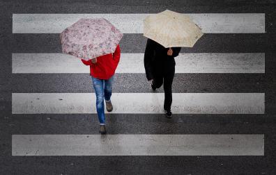 Dos peatones cruzan bajo sus paraguas un paso de peatones en Pamplona este martes.