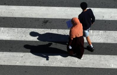 Dos personas caminan sobre un paso de peatones frente al Parlamento de Navarra, en Pamplona