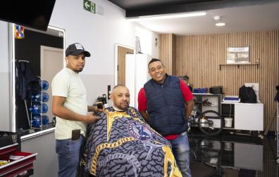 Eric Soto y Joel Alexander de la Cruz, barberos de MLB Barbershop (Sarriguren), atendiendo a su cliente Ricardo Herrera
