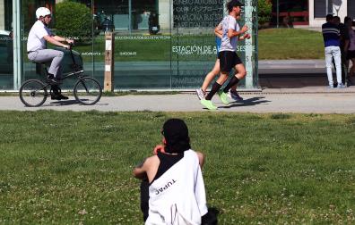Una persona se sienta y observa pasar a otras en una tarde solada la Vuelta del castillo de Pamplona /