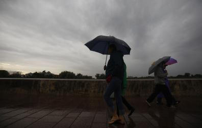 Unas personas tratan de protegerse de la lluvia y de las rachas de viento en Córdoba /