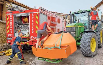 Un bombero ayuda a llenar de agua el depósito del tractor a dos vecinos en Orrio