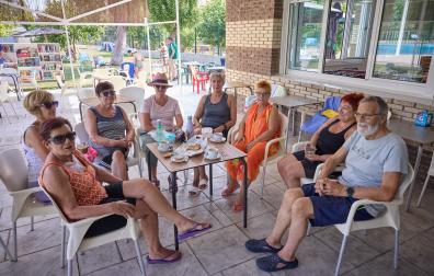 De izq. a dcha.: María Antonia Alfaro, Montse Boteargues, María Jesús Ábrego, Inma Bueno, Rufo Ayerbe, Mari Carmen del Río, María José González y Natxo Salinas desayunan en la piscina municipal de Miranda de Arga, con la biblioteca móvil al fondo.