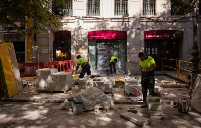 Tres operarios colocan las planchas de hormigón en la acera norte del paseo, junto a una sucursal bancaria y a un bar restaurante