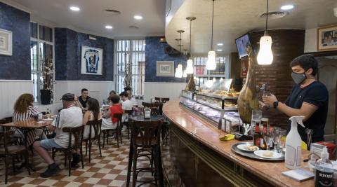 Un camarero del bar La Estrella sirve bebidas en el interior del local con varios clientes sentados. Un camarero del bar La Estrella sirve bebidas en el interior del local con varios clientes sentados.