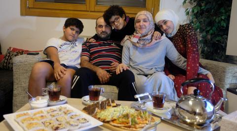 De izquierda a derecha: Ahmad, Jalal, Rafiq, Hadel y Hala, en el salón de su casa frente a una mesa con comida tradicional de su país