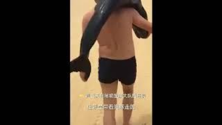 Graban a un hombre con un delfín al hombro paseando por una playa china