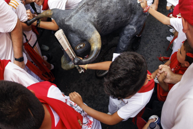 Un grupo de niños corre por delante de un toro de cartón en la Cuesta de Santo Domingo, Pamplona, durante el encierro 'txiki' que se ha celebrado este martes a mediodía y en el que, al tratar de ser lo más real posible al encierro grande, también se canta al santo y se disparan cohetes desde el corral para avisar de la salida de la manada compuesta por seis toros y tres bueyes sobre ruedas.