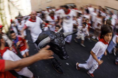 Un grupo de niños corre por delante de un toro de cartón en la Cuesta de Santo Domingo, Pamplona, durante el encierro 'txiki' que se ha celebrado este martes a mediodía y en el que, al tratar de ser lo más real posible al encierro grande, también se canta al santo y se disparan cohetes desde el corral para avisar de la salida de la manada compuesta por seis toros y tres bueyes sobre ruedas.