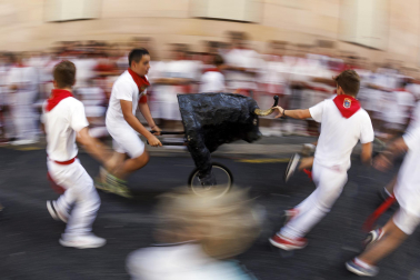 Un grupo de niños corre por delante de un toro de cartón en la Cuesta de Santo Domingo, Pamplona, durante el encierro 'txiki' que se ha celebrado este martes a mediodía y en el que, al tratar de ser lo más real posible al encierro grande, también se canta al santo y se disparan cohetes desde el corral para avisar de la salida de la manada compuesta por seis toros y tres bueyes sobre ruedas.